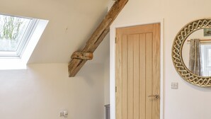 A room with a sloped ceiling, a wooden door, a round mirror with a geometric frame, and a window. - 2 bedroom accommodation in Corwen (Corwen)