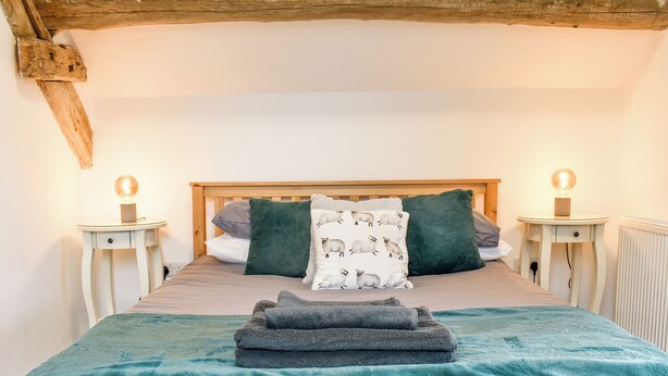 A bedroom with a wooden headboard, two bedside tables with lamps, a bed with a teal blanket, and a pillow with a sheep pattern. - 2 bedroom accommodation in Corwen (Corwen)