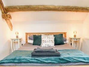 Un dormitorio con cabecera de madera, dos mesitas de noche con lámparas, una cama con manta color turquesa y un cojín con estampado de ovejas.
