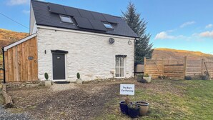 A white building with a black roof, a wooden door, and a sign indicating 'The Barn Car Parking'. - 2 bedroom accommodation in Corwen (Corwen)