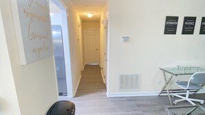Un pasillo que conduce a una escalera, un bote de basura y una mesa de vidrio con sillas.