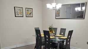 Un comedor con una mesa rectangular, seis sillas, una araña y dos cuadros con motivos florales en la pared.