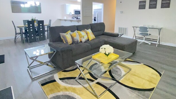Una sala moderna con un sofá gris, una mesa de centro de vidrio y un tapete amarillo estampado.