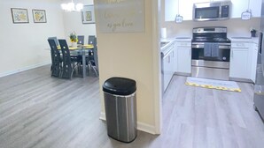 Una cocina moderna con electrodomésticos de acero inoxidable, un comedor con mesa y sillas, y un bote de basura.