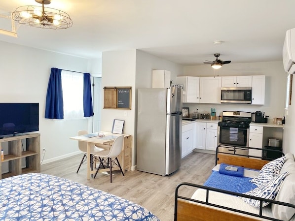 A compact living space with a kitchenette, a bed with patterned bedding, a desk with a chair, and a television.