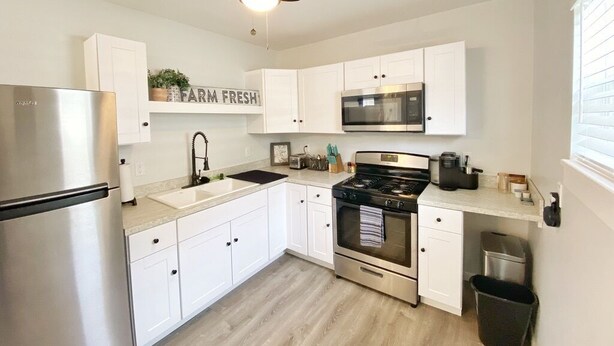 Una cucina moderna con pensili bianchi, elettrodomestici in acciaio inossidabile e una ventola a soffitto.