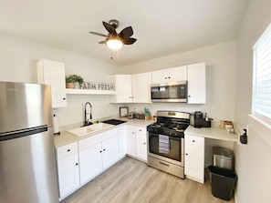 A modern kitchen with white cabinets, stainless steel appliances, and a ceiling fan.