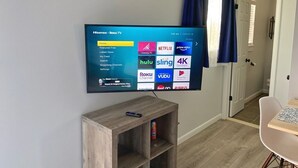 Una TV a schermo piatto montata a parete mostra l'interfaccia Roku TV con diverse icone di servizi di streaming.