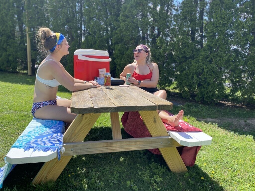 Dos personas sentadas en una mesa de picnic de madera al aire libre, con una nevera al fondo.