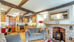 A cozy living room with a fireplace, wooden beams, and a kitchen in the background. - Nans Cottage - UK43350 (Whitby)