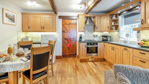 A kitchen with wooden cabinets, a dining table with chairs, a stove, and a microwave. - Nans Cottage - UK43350 (Whitby)