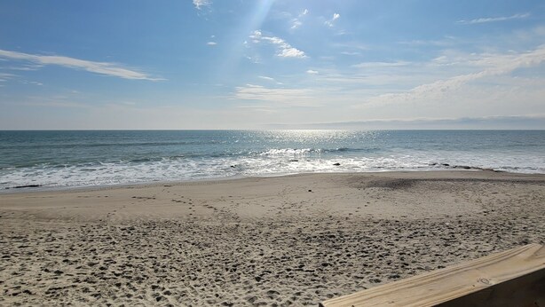 A beach with a wooden bench and footprints in the sand.