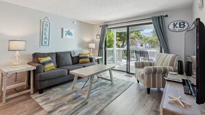 A living room with a grey sofa, a wooden coffee table, striped armchairs, and a large sliding glass door to the outside.