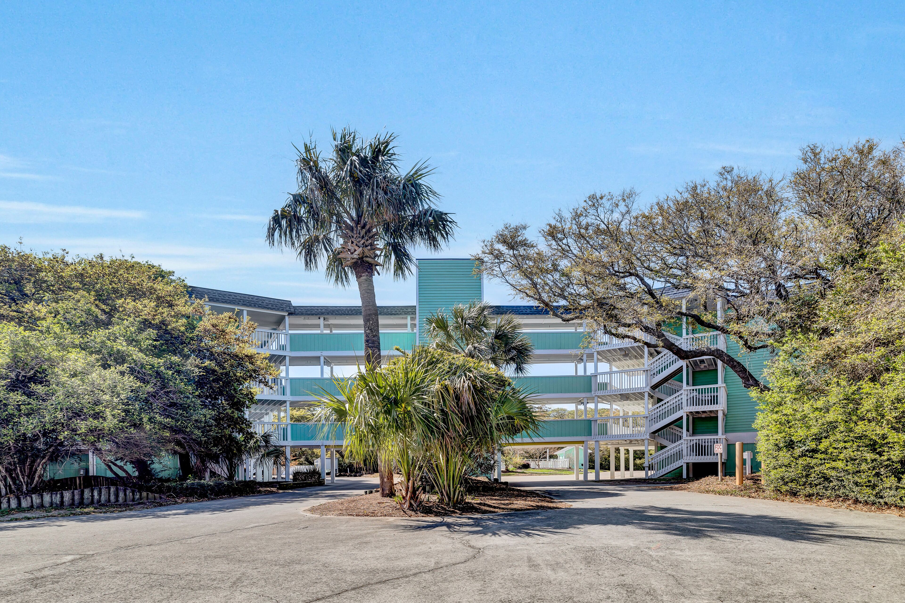 A multi-story building with a green facade, a palm tree, and surrounding greenery.