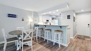 A modern kitchen with white cabinets, a central island with stools, and a dining table with chairs.
