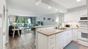 A modern kitchen with white cabinets, a built-in oven, and a dining area with a table and chairs.