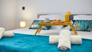Una cama bien hecha con una manta azul, una bandeja de madera con croissants, una taza de café y un vaso de zumo de naranja.