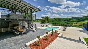 Un patio moderno al aire libre con piscina, zona de comedor y vistas a un viñedo.