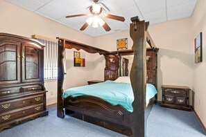 Relax in comfort with a four-poster bed, dresser, and bedside table, surrounded by framed artwork and a carpeted floor.