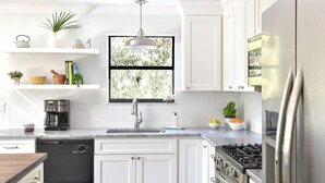 Een moderne keuken met witte kastjes, een ingebouwde vaatwasser, een roestvrijstalen koelkast, een gasfornuis en een raam met uitzicht op groen.