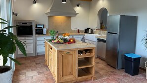 Una cucina con isola centrale, mobili in legno, frigorifero in acciaio inox e pavimento piastrellato.
