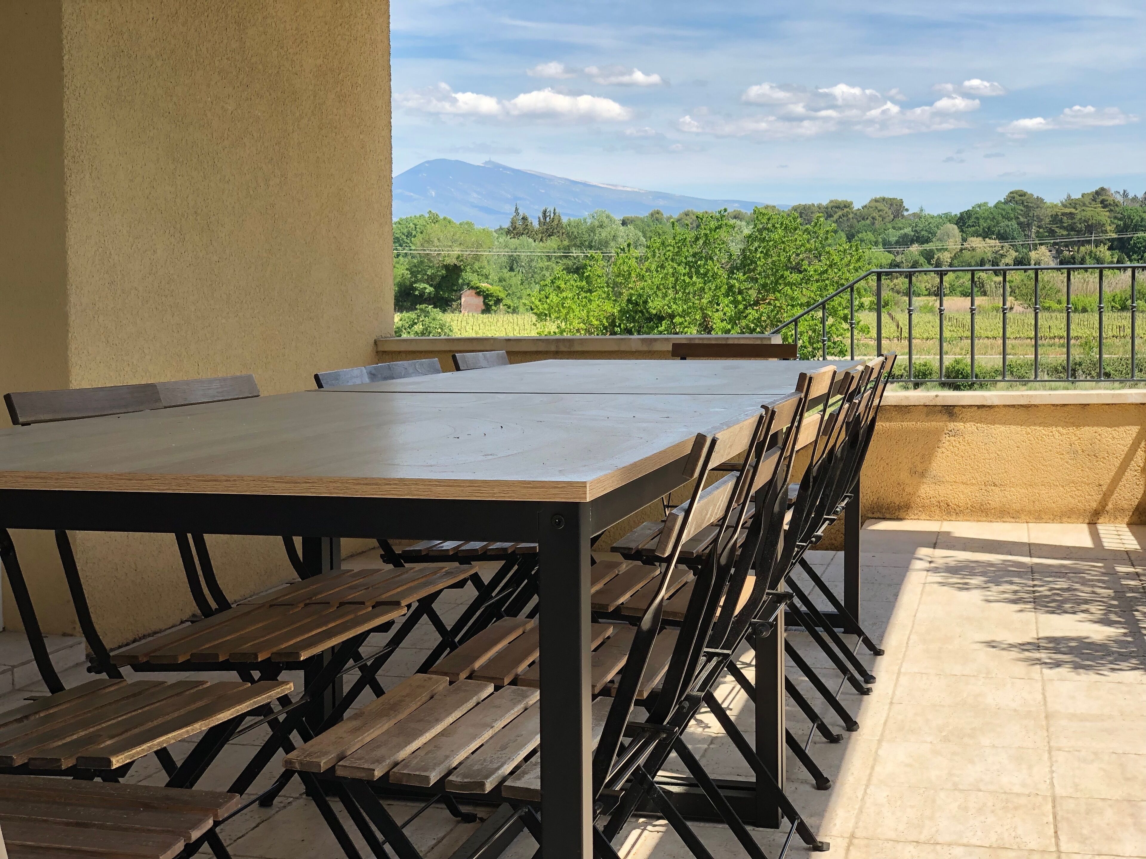 A terrace with a wooden table and chairs, a view of a mountain, and a railing.