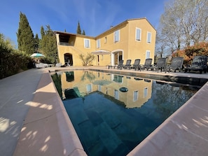 Une piscine dont l’eau est si claire qu’elle reflète parfaitement l’environnement, un bâtiment doté d’un balcon et des sièges à l’extérieur.