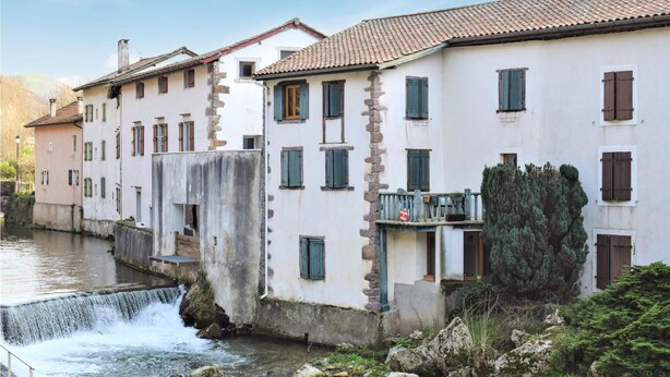 Un edificio histórico con fachada de piedra, una pequeña cascada y un río.
