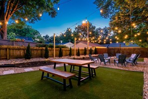 Un jardin avec une table et des chaises en bois, entouré d’une clôture en bois et d’arbres.