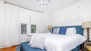 A bedroom with a large bed, two bedside lamps, a window with curtains, and a bedside table with a lamp. - Luxury 4BR|KING|Epic Backyard|HOT TUB|Fire Pit (Louisville)