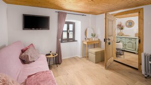 Ein gemütliches Zimmer mit Holzbalkendecke, einem Bett mit rosa Bettwäsche, einem kleinen Tisch mit einer Pflanze, einem Spiegel und einem grünen Schrank.