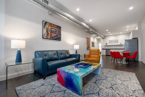 Uma sala de estar moderna com um sofá azul, uma mesa de centro colorida e uma área de jantar com cadeiras vermelhas.