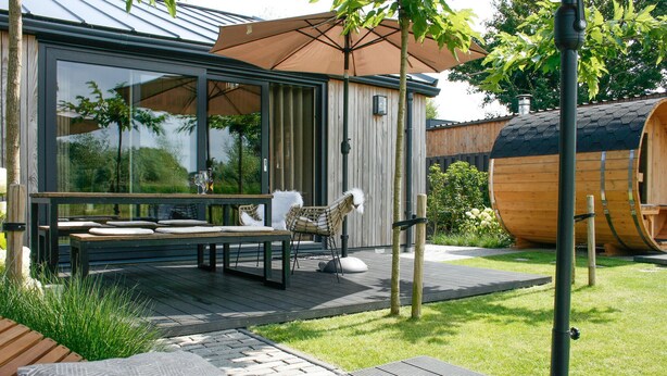 A modern outdoor patio with a glass enclosure, a wooden deck, and a seating area with a table and chairs.