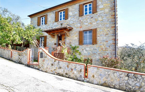 A stone building with a stone wall, wooden shutters, and a small porch.