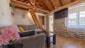 A cozy living room with a wooden ceiling, a stone wall, a grey sofa, a wooden table, and a staircase. - Gorgeous home in Bruska with private swimming pool, can be inside or outside (Bruska)