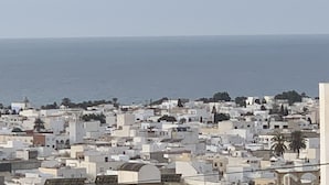 Un paisaje urbano costero con edificios densamente agrupados, algunos con techos planos y otros con estructuras abovedadas, que da al mar.