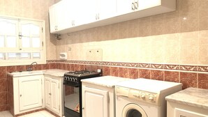 Una cocina con armarios blancos, estufa a gas, lavadora y salpicadero de azulejos.
