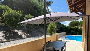 A patio with a table and chairs, a pool, and a covered area with an umbrella.