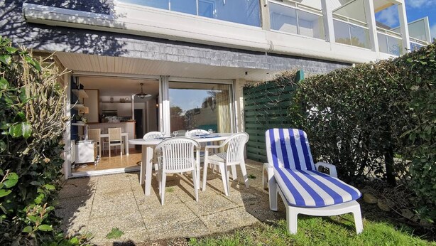 A modern house with a patio area featuring a dining table, chairs, and a striped lounge chair. - CARNAC - Apartment 2 rooms - 4/5 persons - Terrace Sea View (CARNAC)