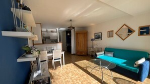 A living room with a sofa, a dining table with chairs, a kitchen area, and a staircase. - CARNAC - Apartment 2 rooms - 4/5 persons - Terrace Sea View (CARNAC)