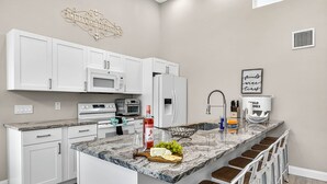 Una cocina moderna con armarios blancos, encimera de granito, horno empotrado, refrigerador y una zona de bar con taburetes.