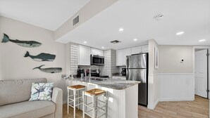 A modern kitchen with white cabinetry, a central island with stools, a microwave, and a refrigerator. - Gulf Shores Plantation-West 1154 (Gulf Shores)