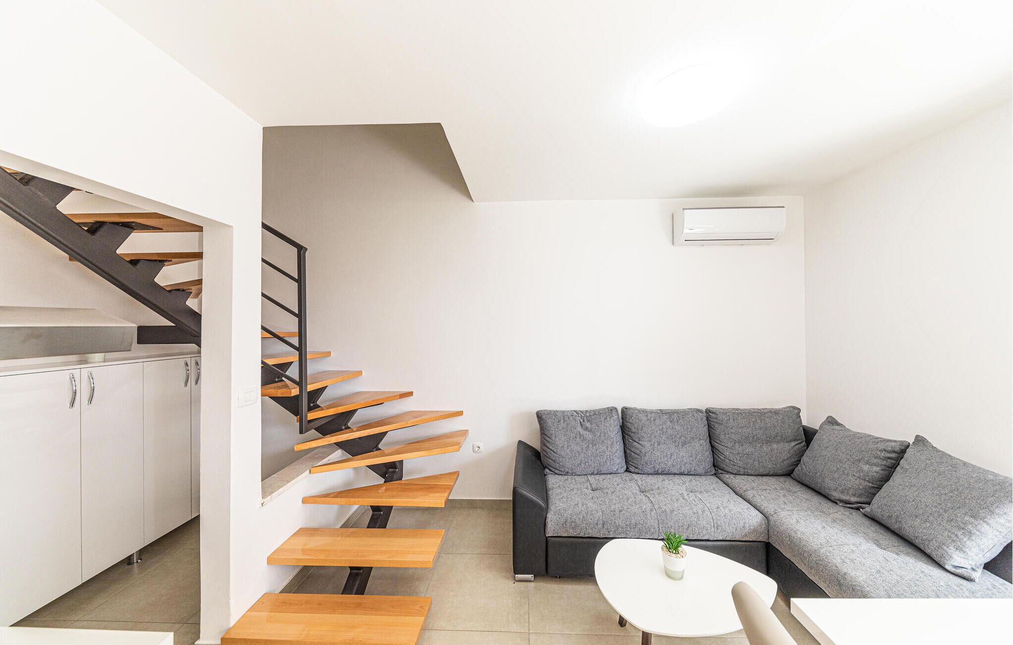 A modern apartment with a staircase, a grey sectional sofa, and a small table with a plant.
