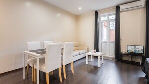 Ein modernes Wohnzimmer mit Esstisch, Stühlen, einer Couch, einem kleinen Couchtisch und einem Fernseher auf einem Schrank.