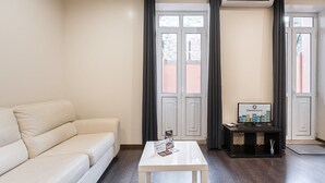 Ein modernes Wohnzimmer mit einem weißen Sofa, einem kleinen weißen Tisch und einem Fernseher auf einem schwarzen Lowboard.