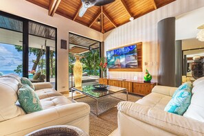 A modern living room with a glass coffee table, leather sofas, and a large TV screen. - Casa Selva Ocean View Luxury Home- 4 Bedroom (Puntarenas Province)