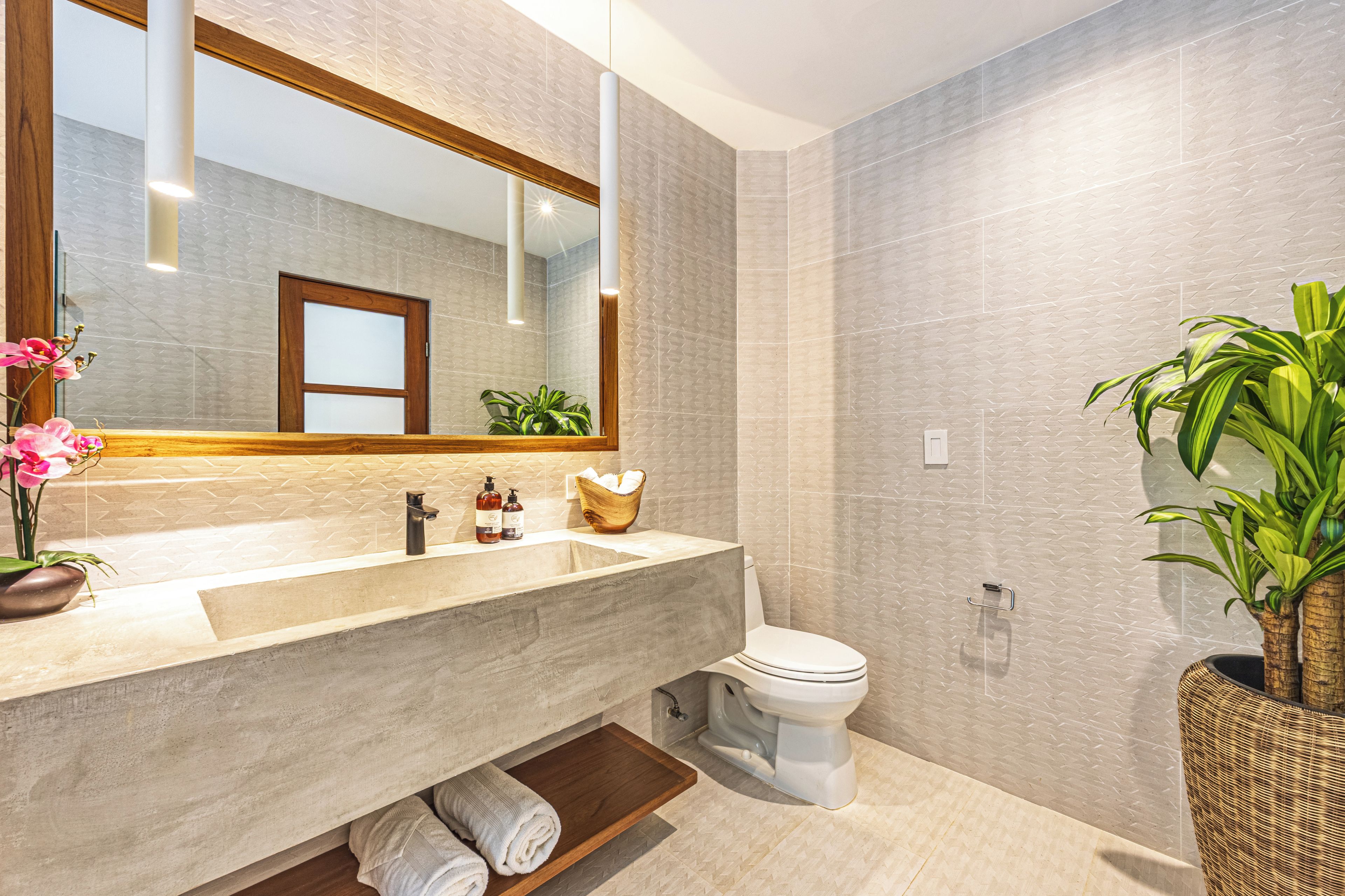 Een moderne badkamer met een grote spiegel, een wastafel, een toilet en een potplant.