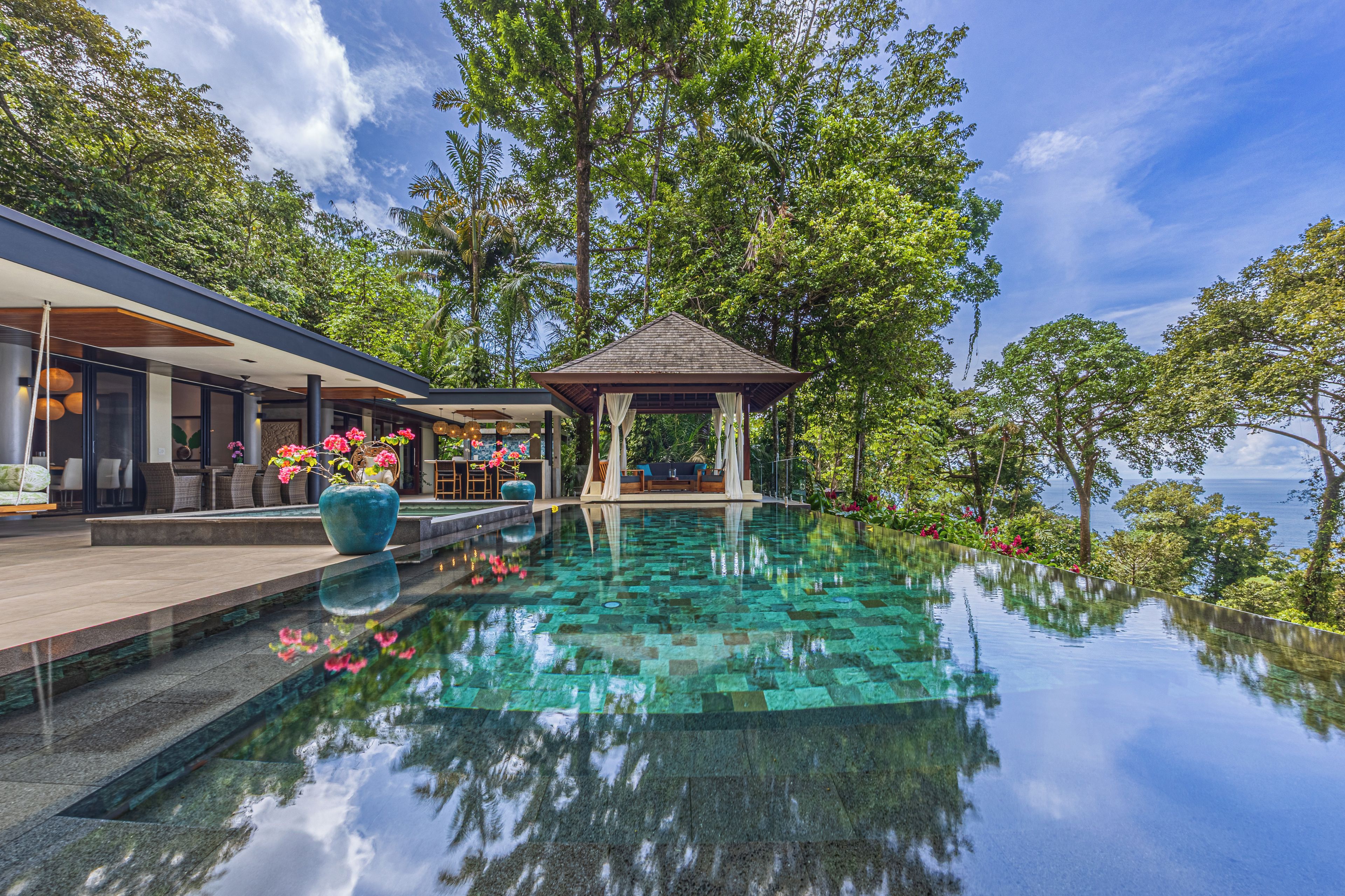 A modern infinity pool with clear water reflecting the surrounding trees and sky.