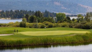 Een golfbaan met een waterpartij op de voorgrond, een vlag op het green en een bebost heuvel in de achtergrond.