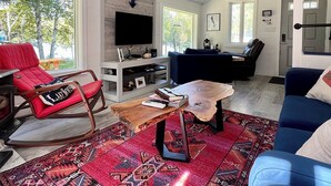 Een woonkamer met een rode schommelstoel, een blauwe bank, een houten salontafel en een vloerkleed met een patroon.